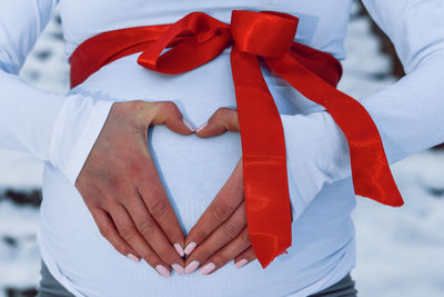 Midsection of pregnant woman forming heart shape on belly