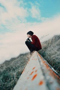 Woman sitting on field against sky