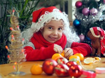 Little girl in santa claus hat rejoices and eats tangerines. on the eve of the meeting of christmas 