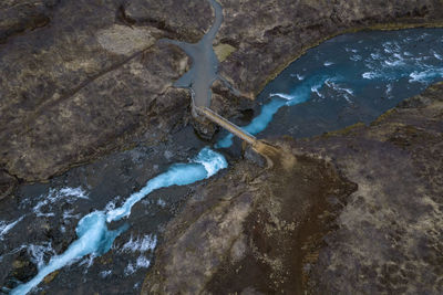 From above drone view of bridge crossing rapid stream with blue water in rough terrain in iceland