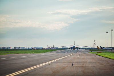 Airplane at airport runway against cloudy sky