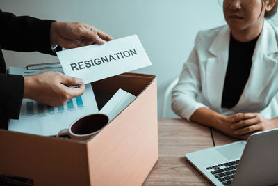 Cropped hands of businesswoman giving resignation letter to manager in office