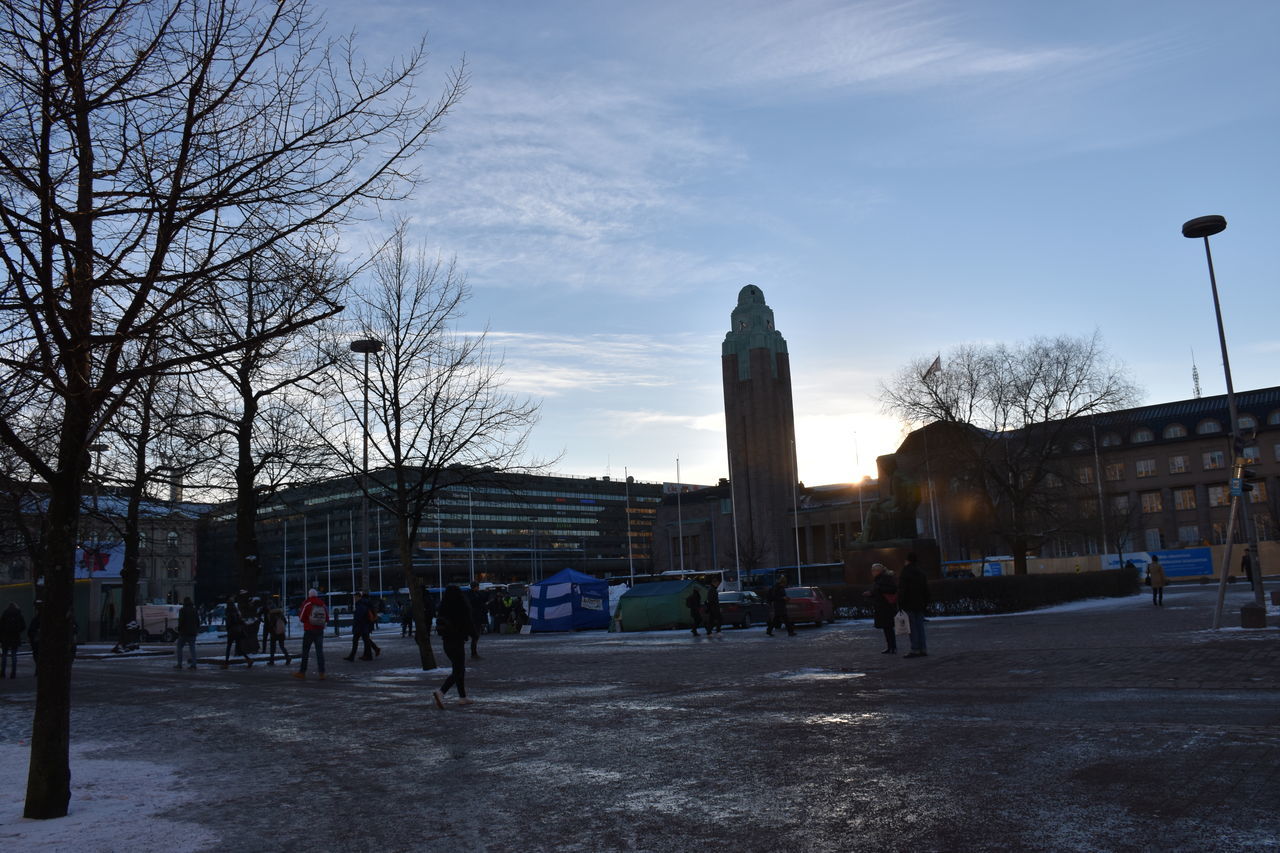 architecture, city, sky, bare tree, built structure, tree, winter, evening, urban area, building exterior, nature, snow, travel destinations, downtown, group of people, street, plant, town square, large group of people, cloud, travel, cityscape, building, tourism, city life, history, the past, crowd, outdoors