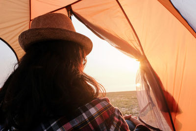 Rear view of woman sitting in tent against sky