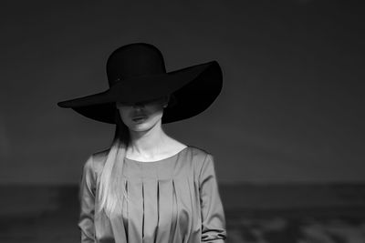 Low section of woman wearing hat standing at beach against sky