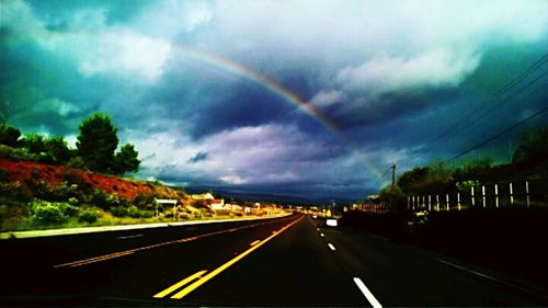 Road passing through highway against cloudy sky