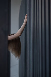 
the girl holds her hands on the bars of the fence, tilting her head