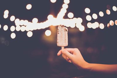 Close-up of hand holding illuminated tea light against sky at night