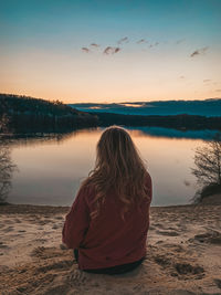 Rear view of woman sitting on beach against sky during sunset