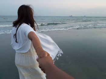 Cropped man holding hand of woman at beach