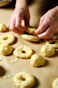 From above anonymous woman making rings from soft dough while preparing doughnuts over table in kitchen