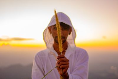 Close-up of man holding umbrella against sea during sunset