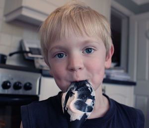 Close-up portrait of cute boy with food covered spoon in mouth at home