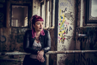 Young woman looking away while leaning on railing in abandoned building