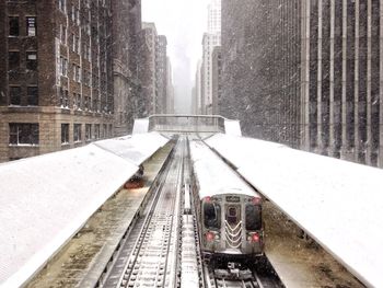 Railroad tracks amidst buildings in city during winter