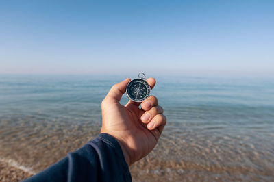 The traveler is looking for direction with a compass on the coastline of the morning sea. 