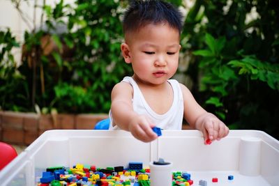 Cute baby boy playing with colorful toys in container against plants