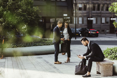 Businessman showing smart phone to female colleague while male coworker surfing net outdoors