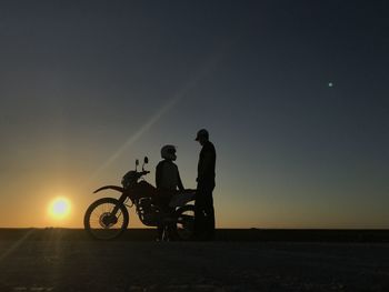 Silhouette men sitting on bicycle against sky during sunset