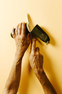 Cropped hands of woman cutting cucumber over beige background