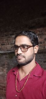 Portrait of young man wearing eyeglasses standing against wall
