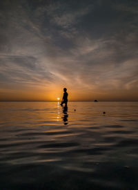 Silhouette man in sea against sky during sunset