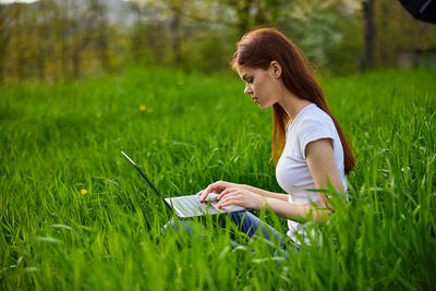 Young woman using laptop while sitting on field