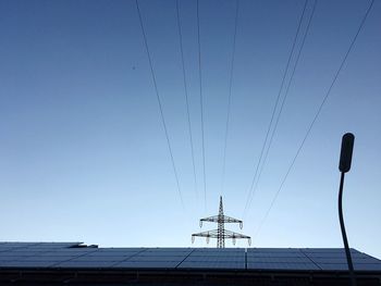 Low angle view of solar panels and electricity pylon against clear blue sky