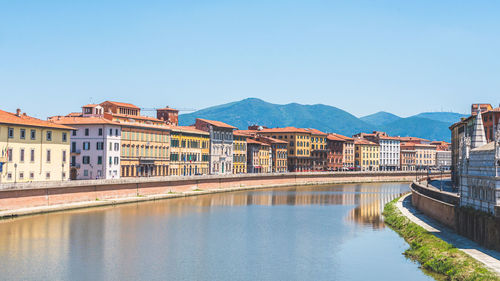 Buildings by river against clear blue sky