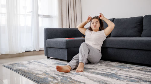 Young woman looking away while relaxing by sofa at home