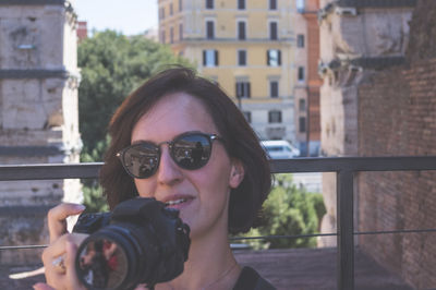 Portrait of young woman wearing sunglasses on retaining wall