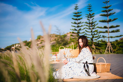 Portrait of young woman sitting on plants against sky