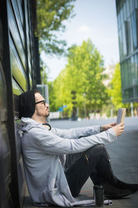 Side view of young man sitting against trees