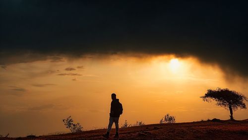 Silhouette man standing on field against sky during sunset