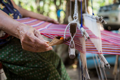 Midsection of woman weaving thread in loom