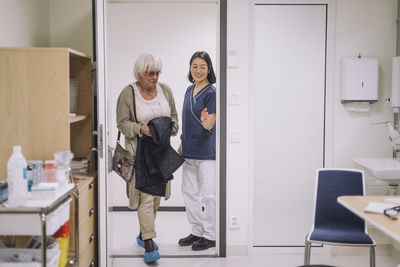 Smiling doctor gesturing to senior patient entering office at hospital