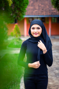 Portrait of smiling young muslim woman standing against building