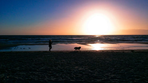 Silhouette people on beach against sky during sunset