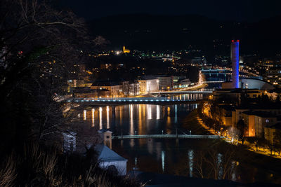 Illuminated bridge over river by buildings in city at night
