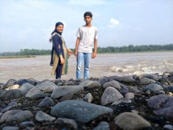 Mother and son standing at beach while stones in foreground