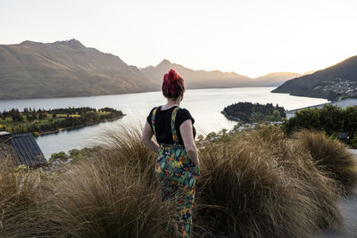 Rear view of woman looking at lake against mountain range