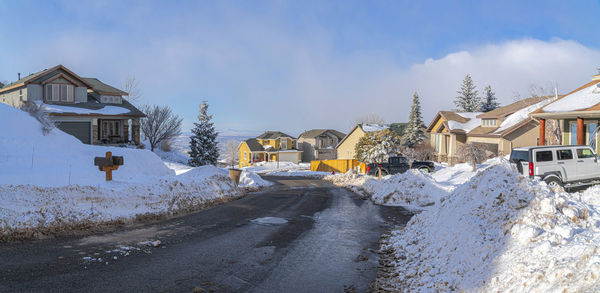 Snow covered houses by road in city against sky