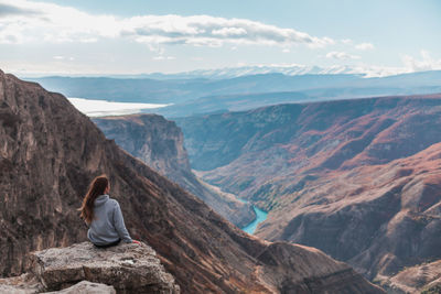 Girl with long brown hair sits and admires the picturesque view of the beautiful canyon. backside