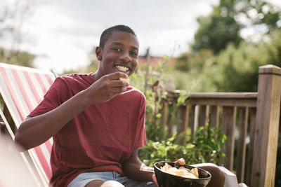 Portrait of smiling boy eating snack while sitting at porch