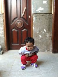Full length of cute boy crouching against door