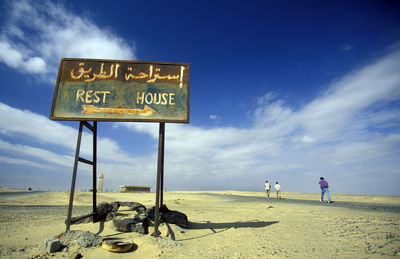 Warning sign on beach against cloudy sky