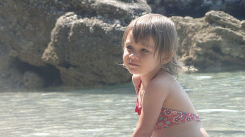 Thoughtful girl in swimwear sitting at beach