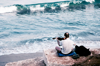 Rear view of man sitting on rock looking at sea