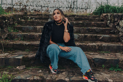 Full length of woman sitting on staircase against wall