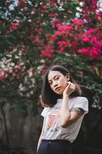 Portrait of young woman standing against pink flowering plants